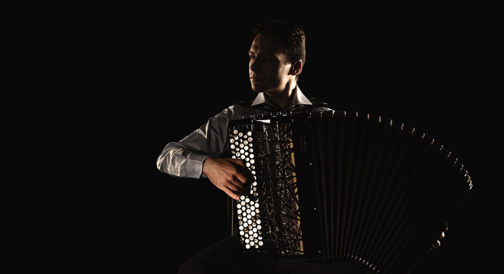 Musician playing the accordion under a spotlight.